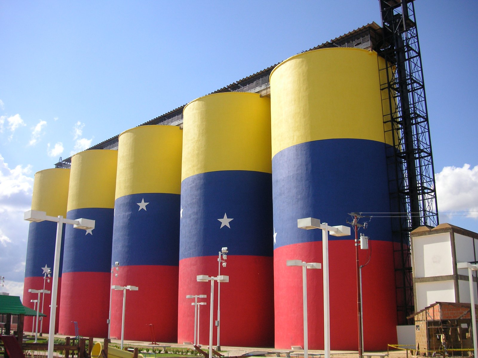 Silos pintados con los colores amarillo, azul y rojo de la bandera de Venezuela, con estrellas blancas, bajo un cielo azul